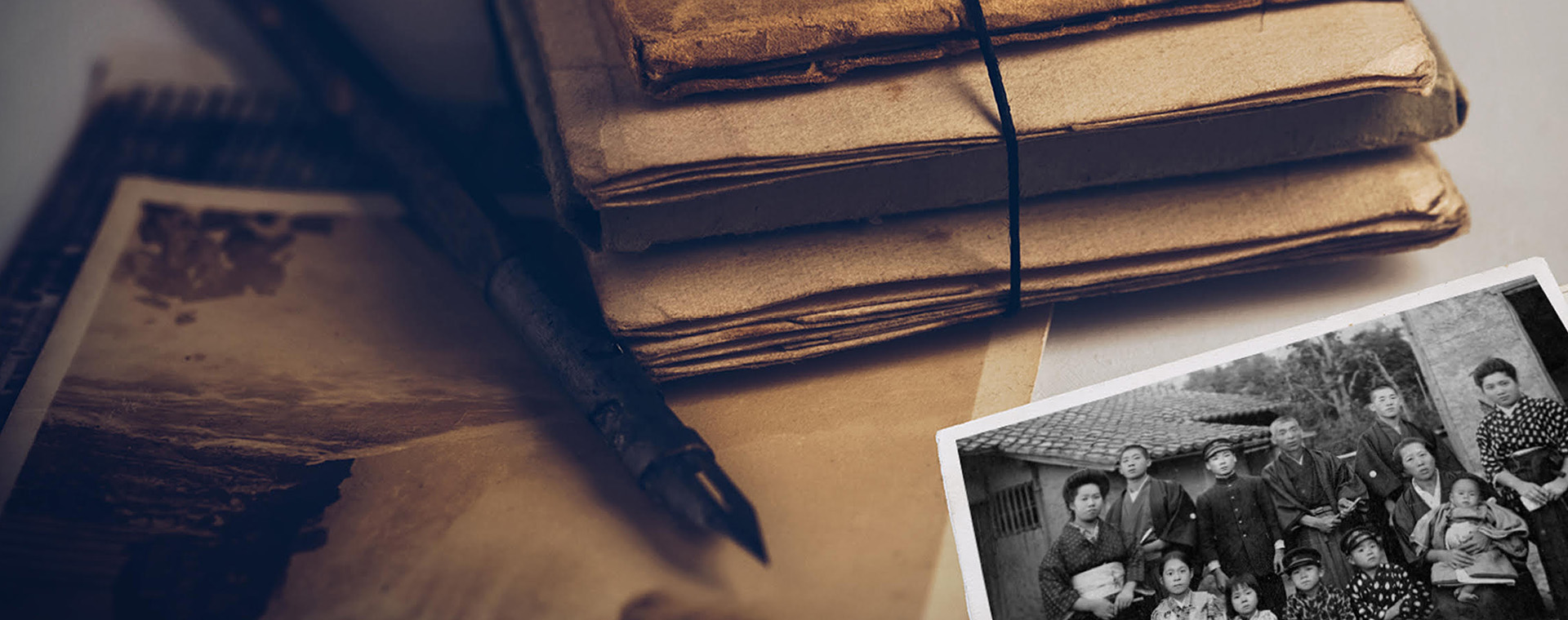 A bundle of sepia-toned documents on a desktop surface with a sepia-toned album and black-and-white photo of people