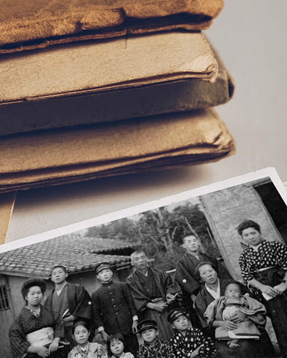A bundle of sepia-toned documents on a desktop surface with a sepia-toned album and black-and-white photo of people