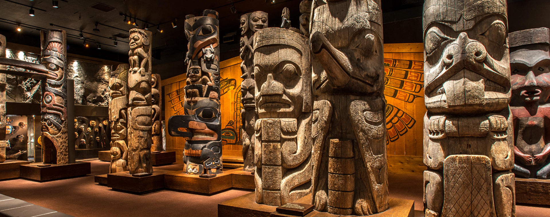 Multiple totem poles standing in a dark room in the Museum