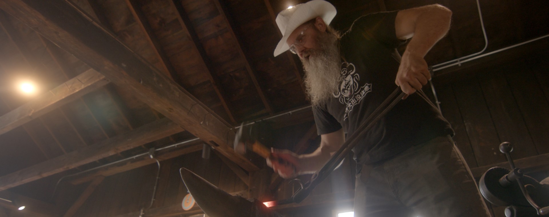 A blacksmith uses tongs to hold a heated piece of metal on an anvil.