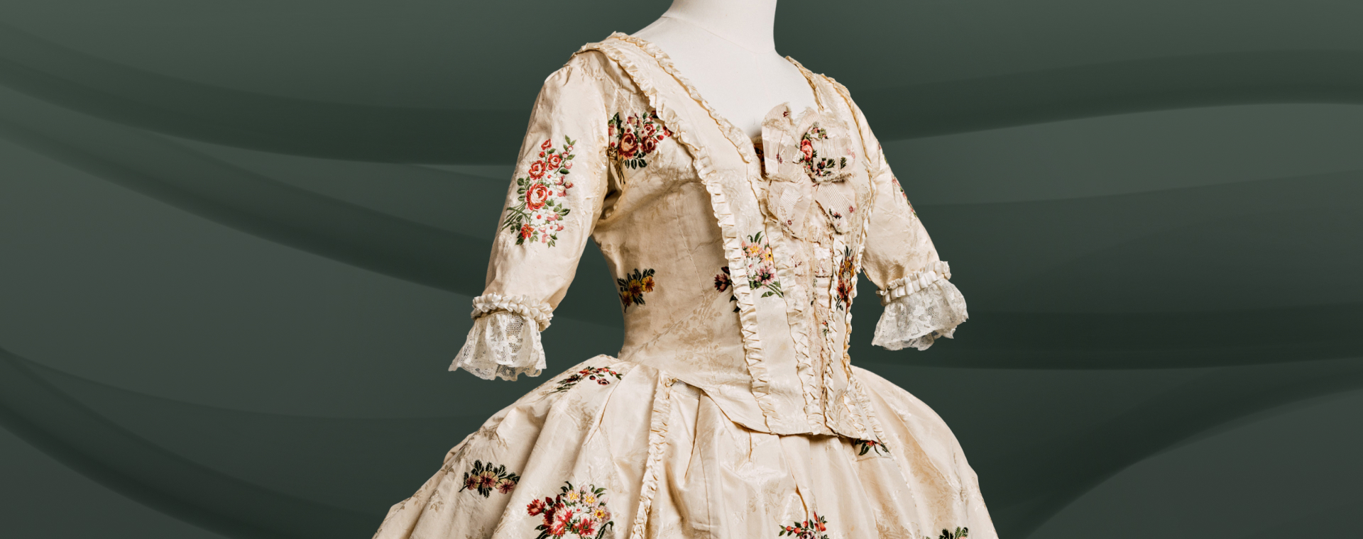 A gown with a bodice fitted at front and back, and a waistline marked by a seam, made of silk decorated with flowers against a white background.
